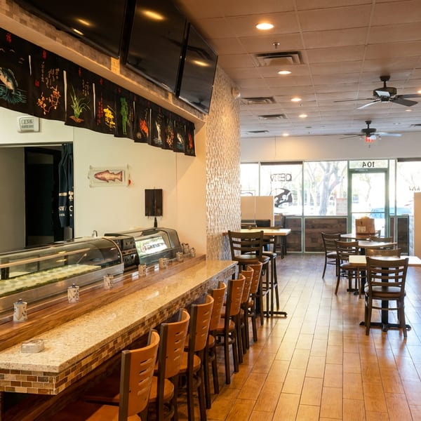 Interior of a sushi restaurant with a sushi bar, dining tables, and booths.