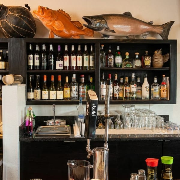 Restaurant bar area with shelves of wine and liquor bottles, beer taps, and kitchen equipment.