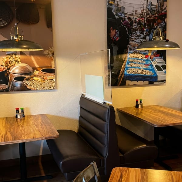 Restaurant interior with dark booths, wooden tables, and large wall art depicting market scenes.